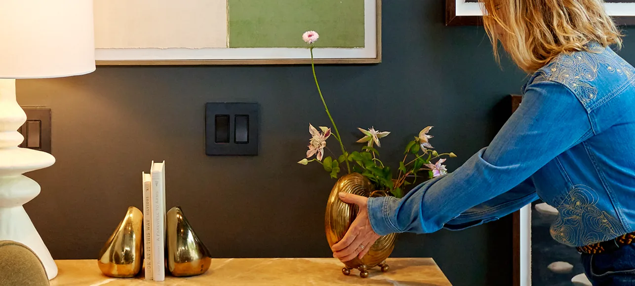 A floral designer styling a console table — a brass vase of blooms beside books and a sculptural lamp