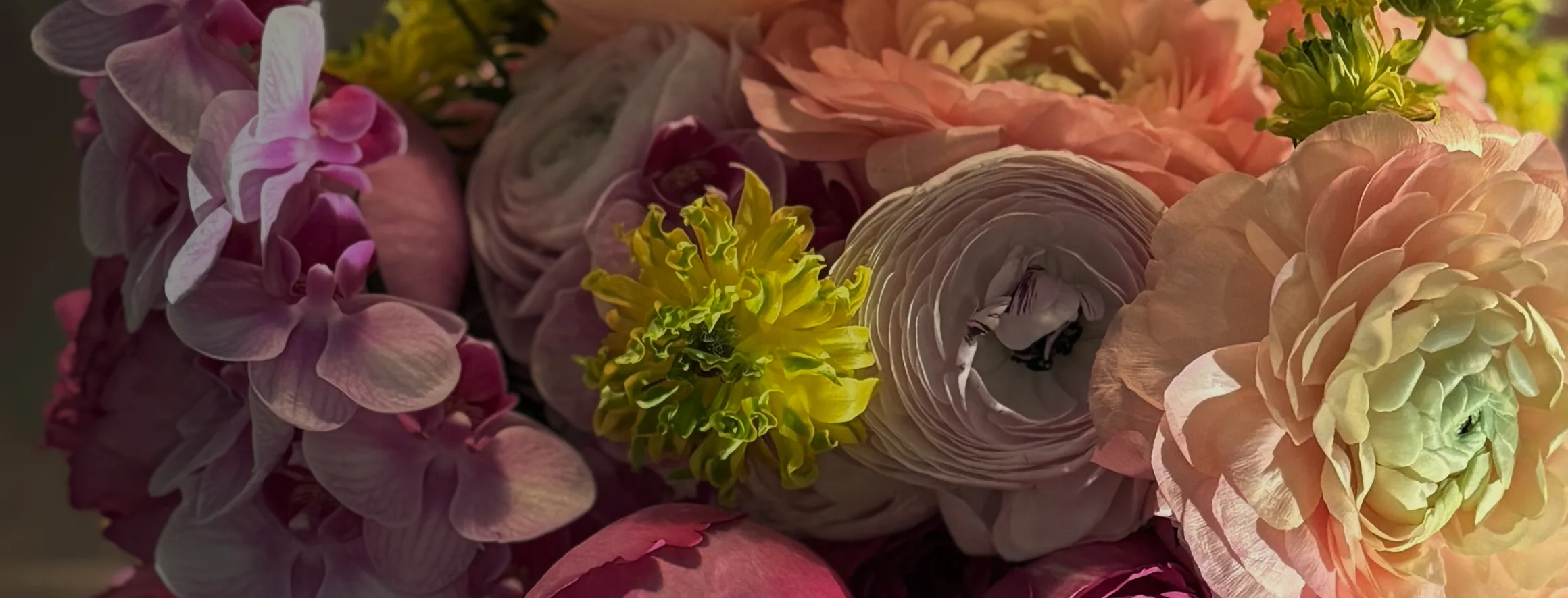 Close-up of a Buunch arrangement: lavender phalaenopsis orchids, peach ranunculus and a chartreuse bloom