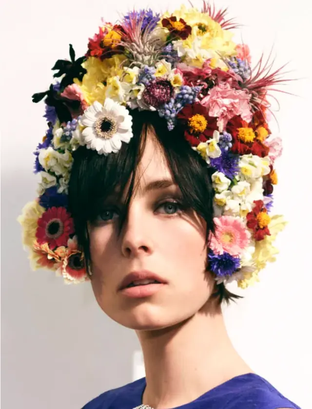 A model in a colorful floral headpiece with a prominent white daisy.
