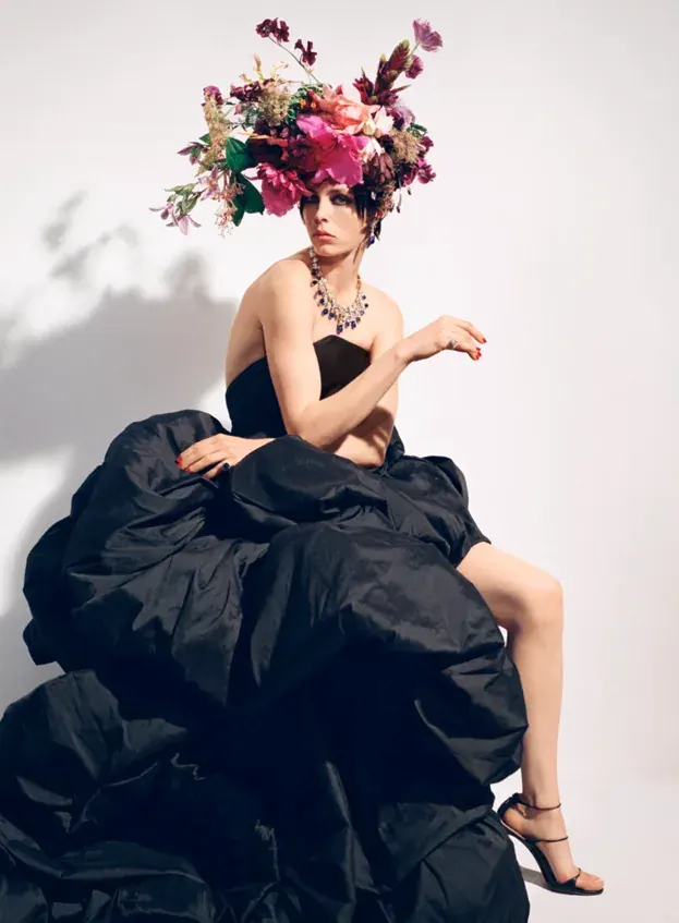 Seated model in a black gown wearing a pink and burgundy exotic floral headpiece.