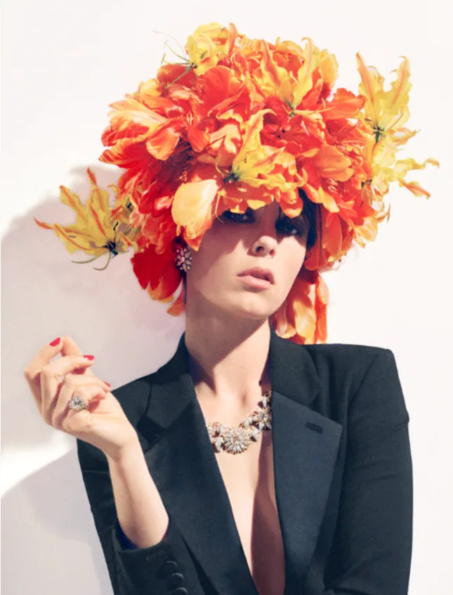 A model in a black suit beneath a headdress of orange poppies