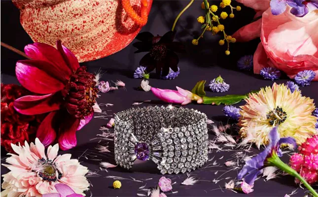 A diamond bracelet resting on a dark arrangement of dahlias and cosmos
