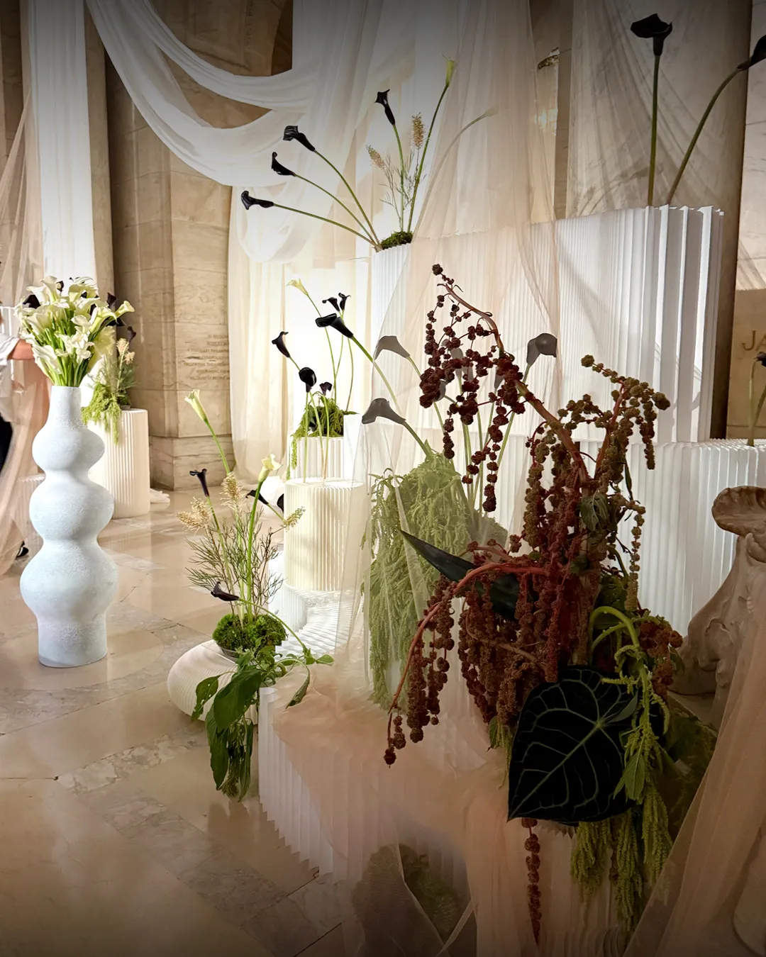 Close-range texture: black callas, trailing amaranth and dark anthurium against white pleated plinths, NYPL wedding