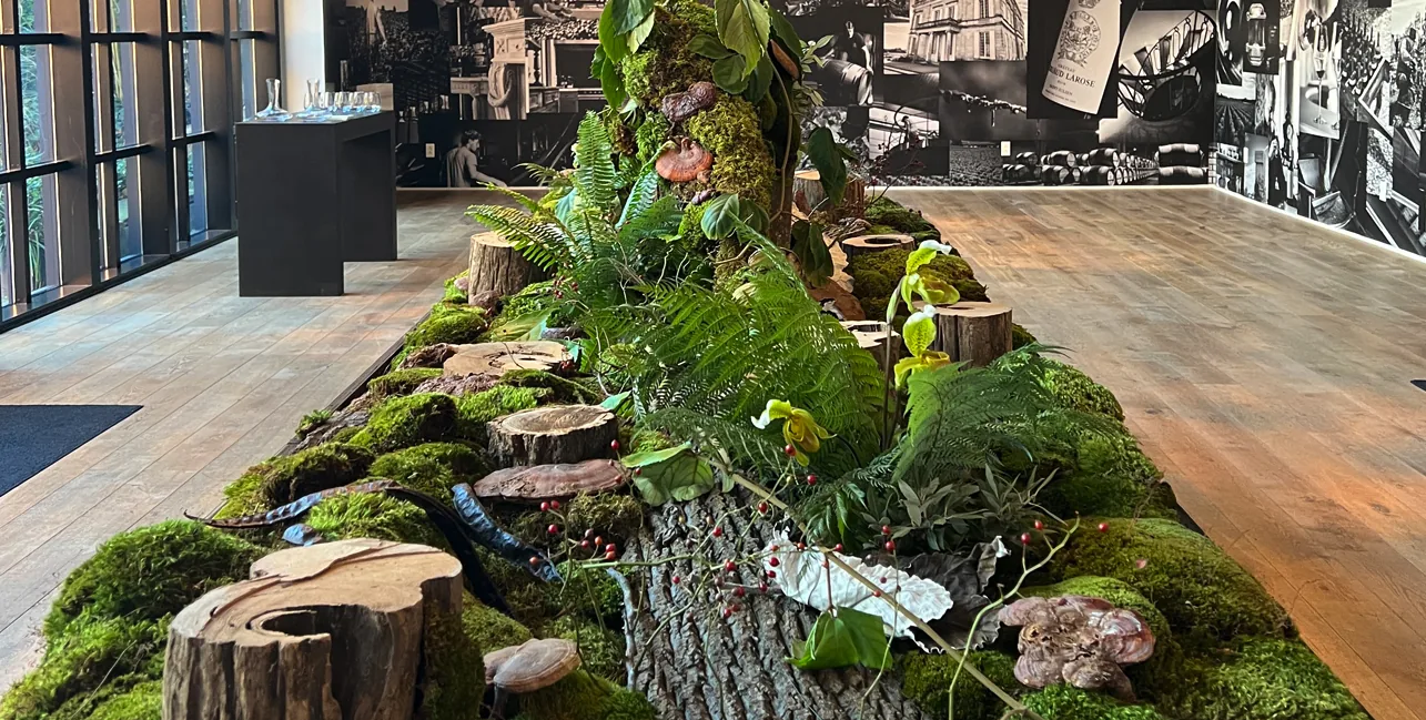 A moss-and-fern table installation with log slices and mushrooms before a photographic mural