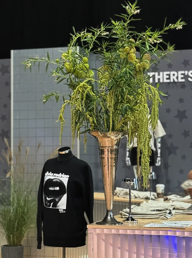 A tall silver vase of trailing greenery beside a mannequin on a star-print backdrop