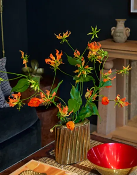 Orange flowers with curved stems in a ribbed bronze vase at the Lemieux et Cie flagship launch.