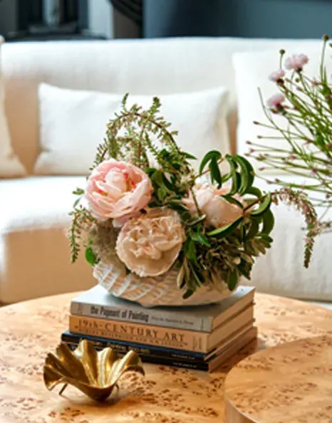 Pale blush garden roses and peonies in a low ceramic bowl on a stack of art books.