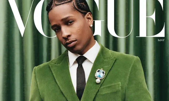A$AP Rocky in a green velvet jacket and jeweled brooch before a green curtain beneath the VOGUE masthead.