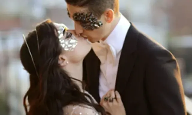 A couple in glittering silver masquerade masks kissing on their wedding day.