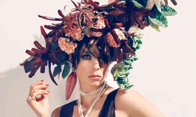 A model in an elaborate dark red and green floral headpiece and layered pearl necklaces.