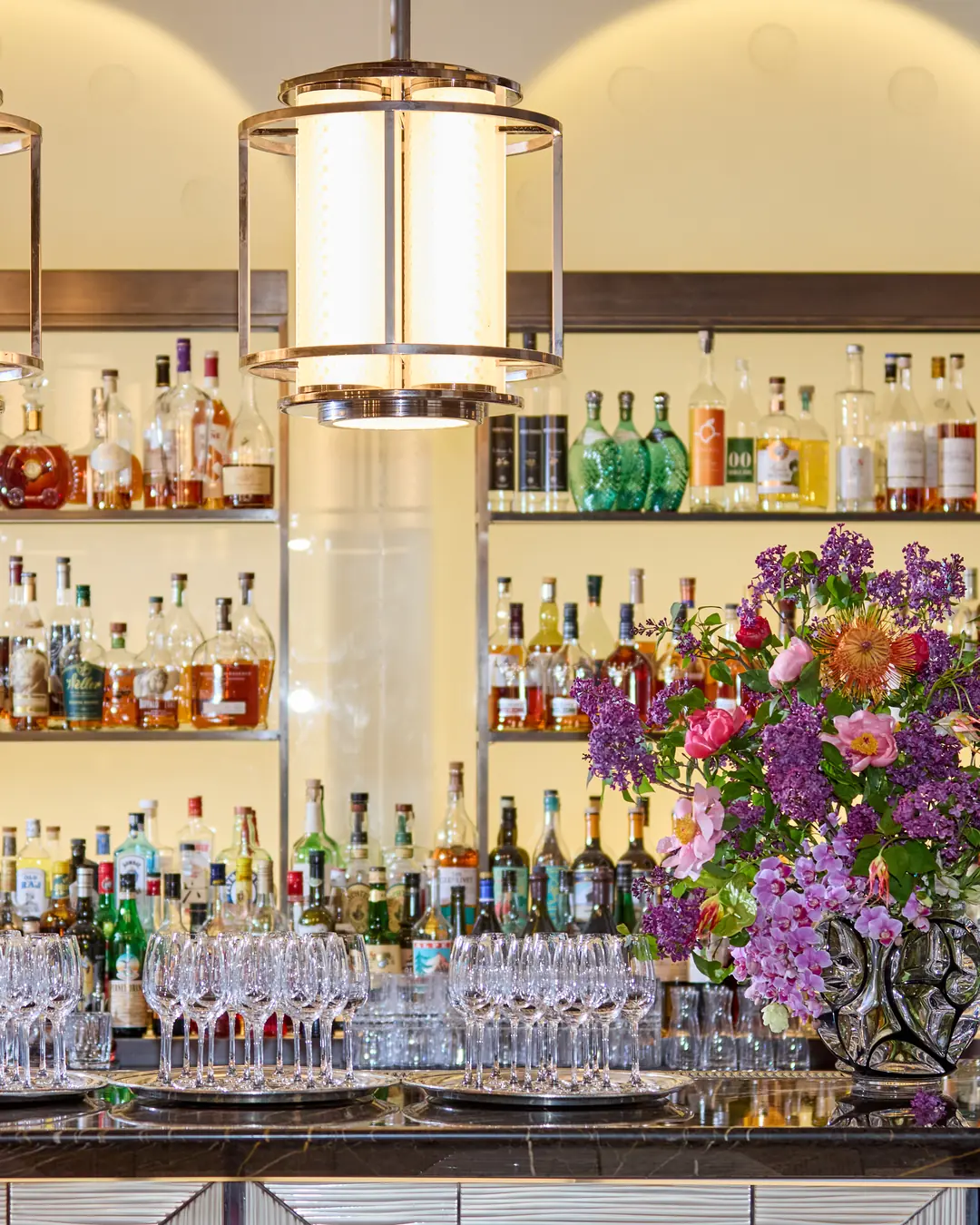 A floral installation of lilac, roses and ranunculus on the bar of a Manhattan restaurant, in warm lamplight