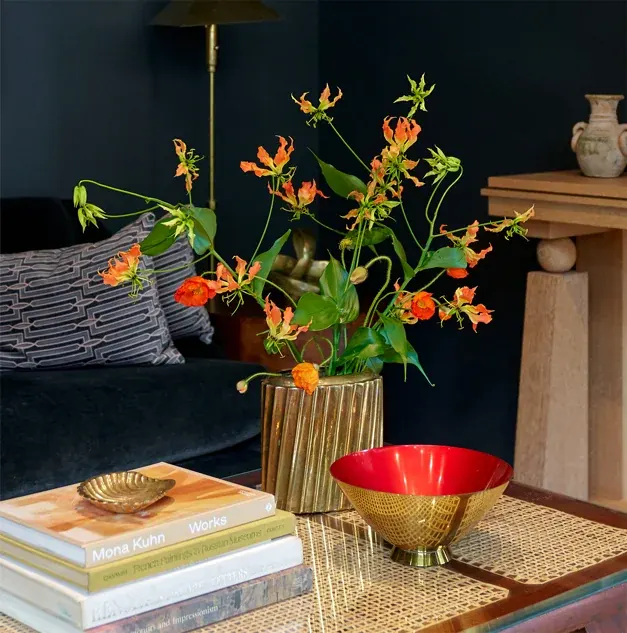 Orange-red flowers with a red bowl on a coffee table in a living room.