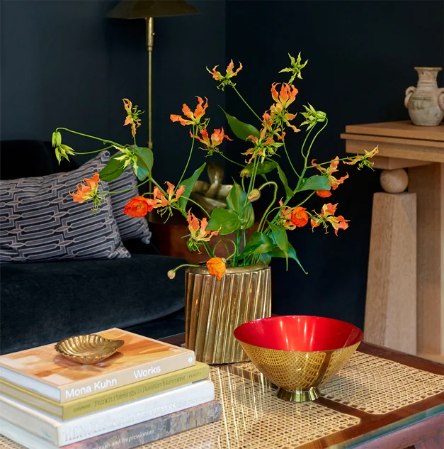 A living room styled with Buunch florals — orange flowers in a gold vase on a coffee table before a dark wall